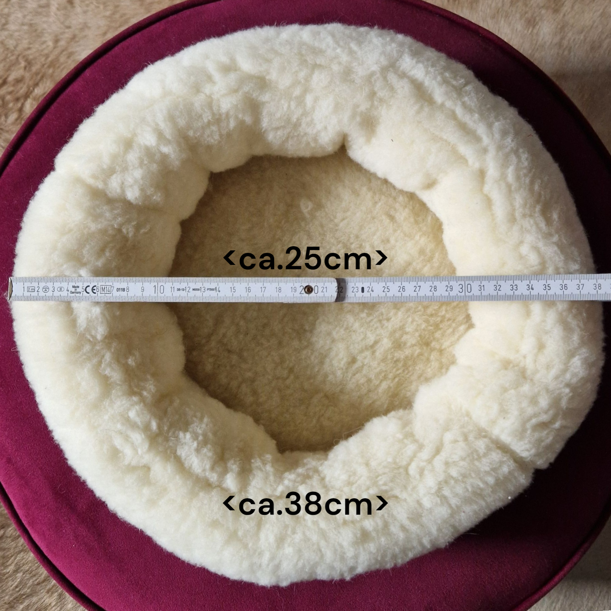 Rundes handgemachtes Hundekissen mit Naturfüllung aus langem Schaffell in Hell-Elfenbein auf rotem Untergrund.